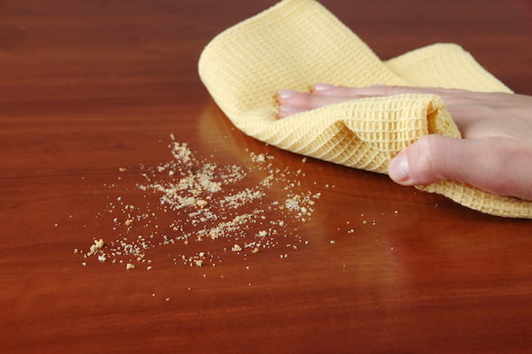 Person wiping hardwood table clean of crumbs using yellow washcloth